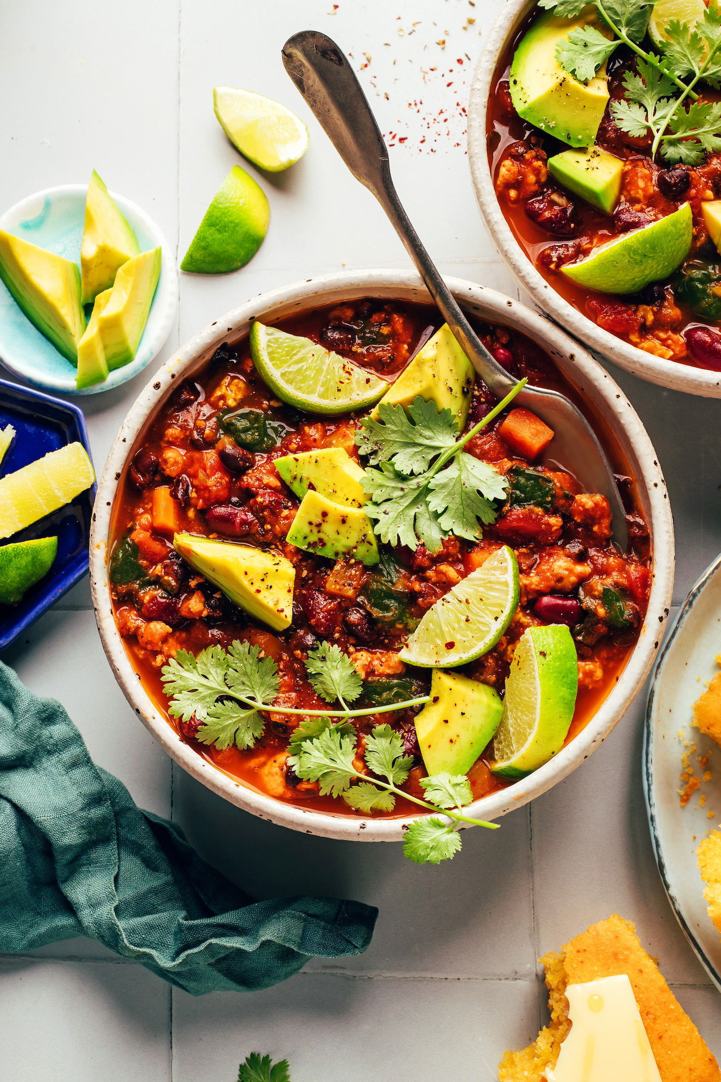 Two bowls filled with pumpkin turkey chili and topped with cilantro, limes, and avocado