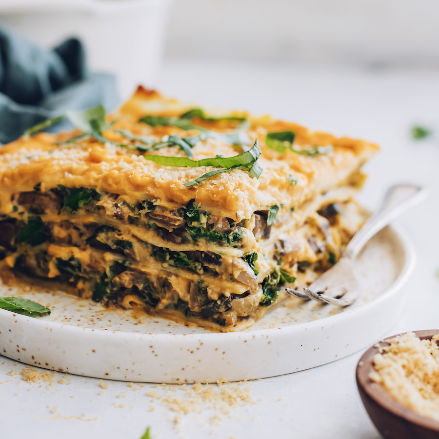 Slice of butternut squash lasagna topped with vegan parmesan and fresh basil