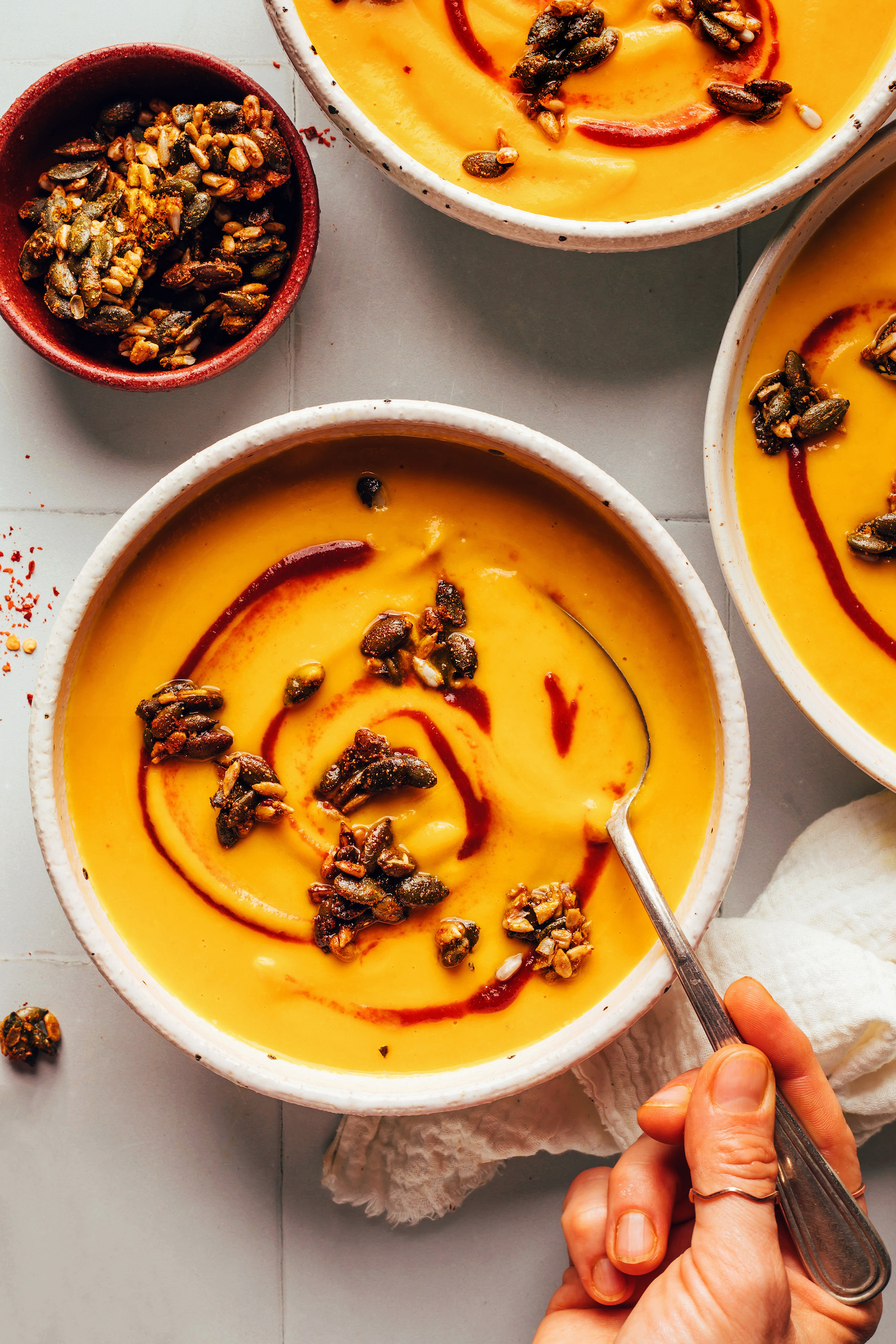 Bowls of creamy vegan carrot ginger soup topped with sriracha and sweet and spicy seeds