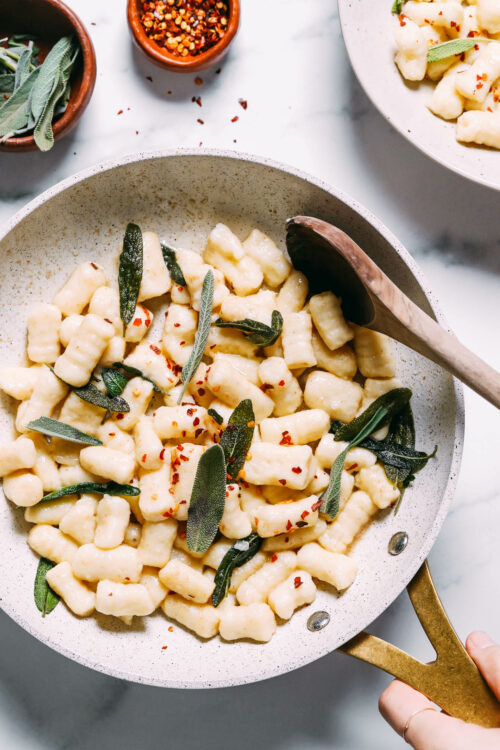 Skillet of gluten-free gnocchi sautéed in vegan butter with crispy sage and red pepper flakes