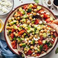 Using a fork and spoon to toss a bowl of Mediterranean cucumber chickpea salad