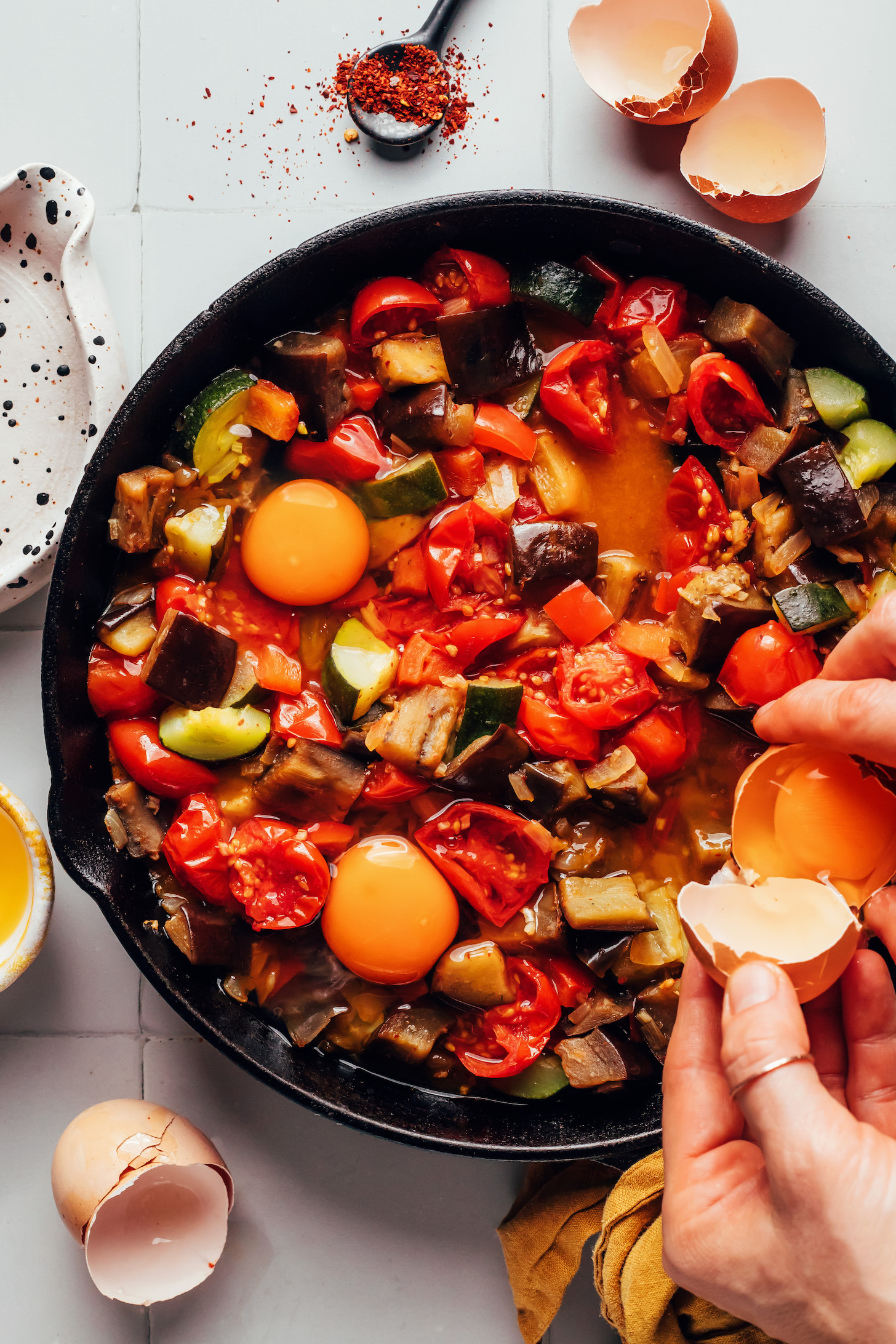 Cracking eggs into a pan of sautéed vegetables