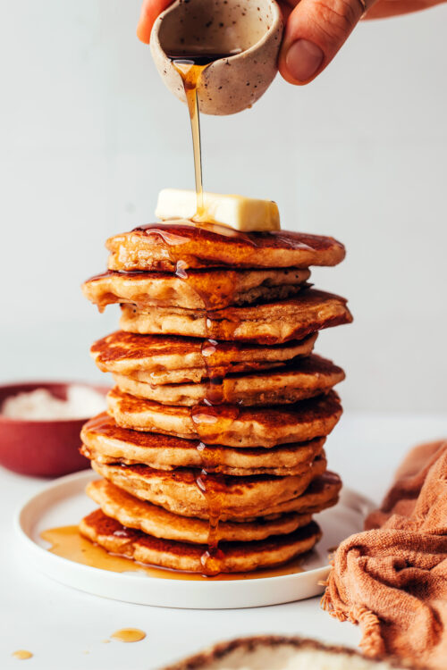 Pouring maple syrup onto a stack of homemade gluten-free pancakes