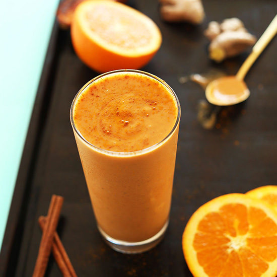Tall glass of our Immune Booster Orange Smoothie recipe on a baking sheet with ingredients to make it