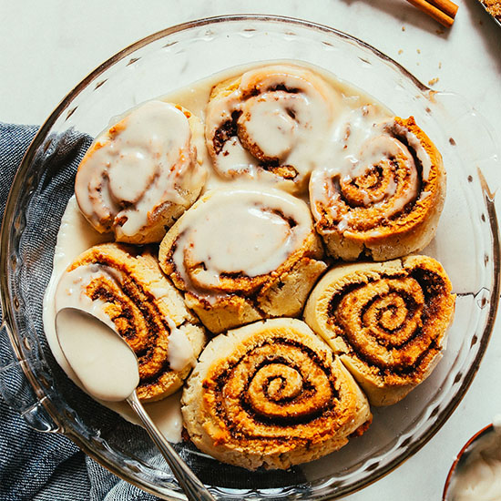 Covering a batch of Vegan Gluten-Free Cinnamon Rolls with icing