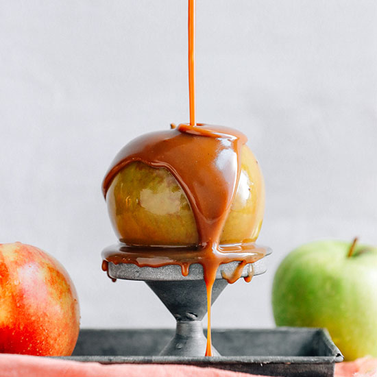 Drizzling Vegan Caramel Sauce onto an apple perched on a metal stand