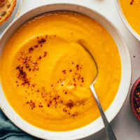 Close up shot of a bowl of creamy vegan carrot soup topped with red pepper flakes