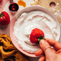 Dipping a fresh strawberry into a bowl of vegan cashew whipped cream