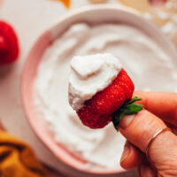 Holding a fresh strawberry dipped in vegan whipped cream