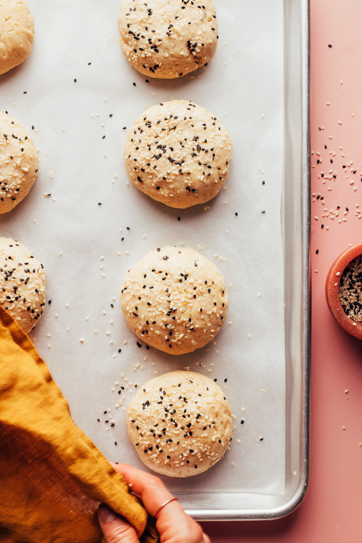 Baking sheet of unbaked hamburger buns topped with sesame seeds